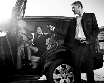 Muškarac u odijelu drži ruku žene koja sjedi unutar crnog SUV-a.